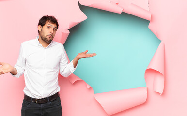 Wall Mural - young handsome indian man doubting or uncertain expression against broken paper hole background