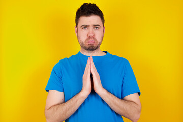 Wall Mural - young handsome caucasian man wearing blue t-shirt against yellow background points at his body, being in good mood after going shopping and making successful purchases