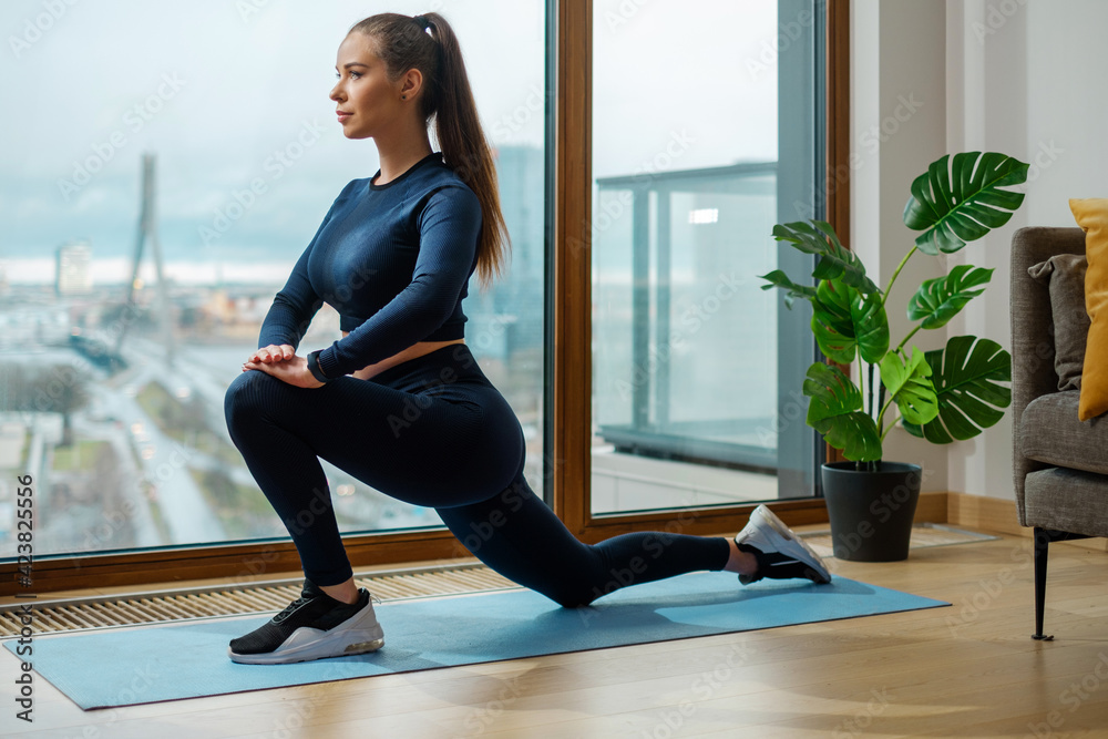 Woman in tracksuit does exercise in warrior pose on mat - obrazy, fototapety, plakaty 