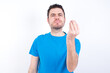 © Roquillo - young handsome caucasian man wearing blue t-shirt against white background angry gesturing typical italian gesture with hand, looking to camera