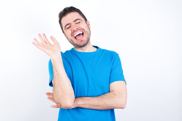 Overjoyed successful young handsome caucasian man wearing white t-shirt against white background raises palm and closes eyes in joy being entertained by friends