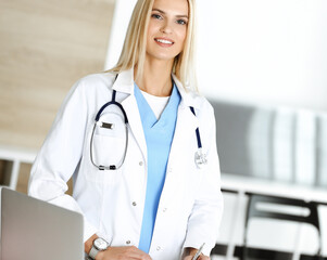 Doctor woman at work in hospital excited and happy of her profession. Blonde physician controls medication history records and exam results while using clipboard. Medicine and healthcare concept