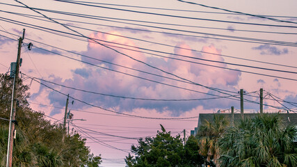 A cumulus cloud turned pink by the setting sun, segmented by the intersecting lines of overhead wires