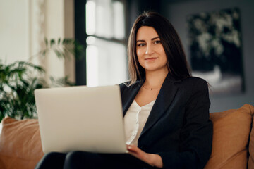 Wall Mural - A confident financial manager. The lawyer is a business woman with a brunette European appearance. Works on a laptop computer. Located in a modern, stylish coworking office.