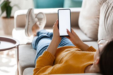 Young woman hold mobile phone in hands, lying on the sofa