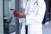 Midsection Of African American Male Doctor Wearing White Coat And Stethoscope Using Digital Tablet