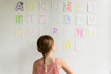 Rear View Of Girl (8-9) Looking At Alphabet On Wall