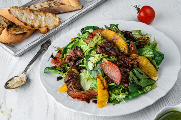 Fresh salad with grilled steak meat, orange, grapefruit, lettuce, greens, spinach, sauce on plate over light wooden background. Healthy food, clean eating, top view