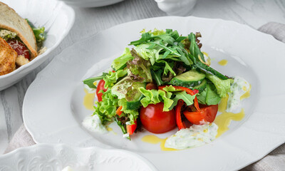 Wall Mural - Fresh green salad with vegetables, tomatoes, arugula, spinach, lettuce, bell pepper, cucumbers and sauce on plate on light wooden background. Healthy food, clean eating, vegan, dieting, close up