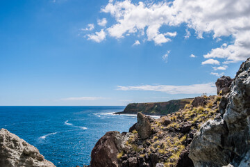 Wall Mural - Mountain hiking trail with cliff rocks with selective focus by the Atlantic Ocean on Terceira Island - Azores PORTUGAL