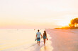 Couple walking on beach during romantic sunset on Florida holiday. Silhouette of young man and woman holding hands happy to be on vacation.