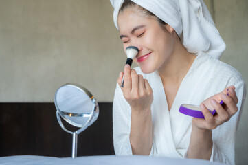 Asian woman using brush for applying concealer on her face. Concealer used to hide different pigments by blending the imperfection into the surrounding skin tone.