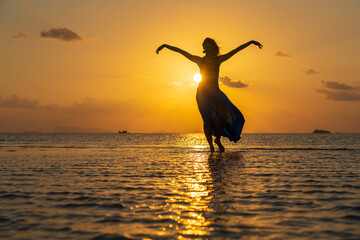 Young beauty girl dancing at tropical beach on sea water at paradise island at sunset. Summer concept