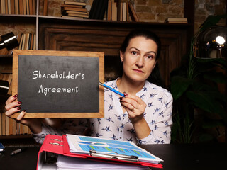 Wall Mural - BusinessWoman holding a chalkboard. Business concept about Shareholder's Agreement with phrase on the sheet.