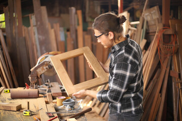 Wall Mural - Young Caucasian carpenter man is making wooden frame in his own garage style workshop for hobby with copy space