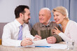 Smiling mature woman and eldery man signing contract with sales manager at home