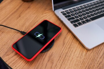 Charging mobile phone battery with wireless device in the table. Smartphone charging on a charging pad. Mobile phone near wireless charger.