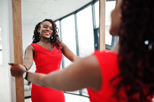 Magnificent Young African Woman In Luxurious Red Dress In A Luxury Apartment Look At Mirror. Beauty, Fashion.