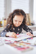 © boytsov - Cute child girl sitting at the table in earphones doing homework drawing using pencils or crayons. Homeschooling or art class concept. Vertical image. High quality photo