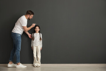 Wall Mural - Father measuring daughter's height near black wall indoors, space for text