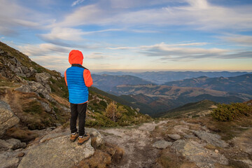 Wall Mural - Young child boy hiker standing in mountains enjoying view of amazing mountain landscape.