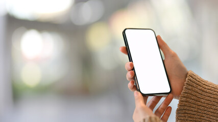 Wall Mural - Female hand holding mock up smartphone with blurred bokeh background