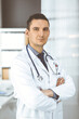© cameravit - Male doctor standing straight with arms crossed in clinic near his working place. Perfect medical service in hospital. Medicine and healthcare concept