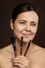 Canvas Print - Beautiful middle aged woman with a makeup brushes on brown background