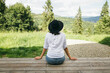 © sonyachny - Stylish hipster woman sitting on wooden terrace on background of sunny mountains hills. Wanderlust