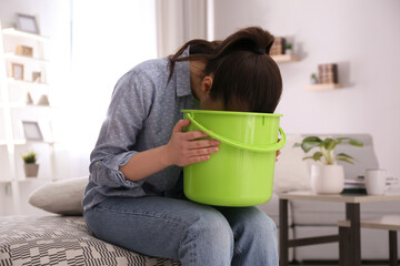 Canvas Print - Young woman with bucket suffering from nausea at home. Food poisoning