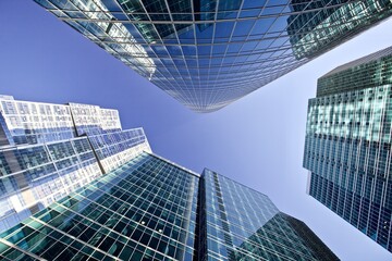 Modern office buildings against bright blue sky. Bottom-up view. Glass facades of skyscrapers with contrasting highlights and reflections. Economy development, finance and business concept. Downtown.