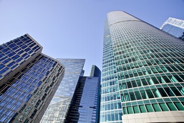 Modern office buildings against bright blue sky. Bottom-up view. Glass facades of skyscrapers with contrasting highlights and reflections. Economy development, finance and business concept. Downtown.