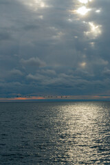 Calm sea and blue sky with white cirrus clouds. The sun shines through the clouds. Birds fly along the sea.