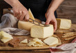 Hands cut pieces of  fresh homemade cheese on a wooden board