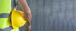 © anut21ng Stock - Construction worker Holding yellow helmet on Cement wall with copy space for banner