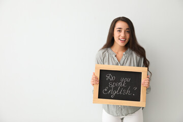 Wall Mural - Young female teacher holding chalkboard with words DO YOU SPEAK ENGLISH? on light background. Space for text