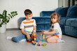 Two young children boy and girl sit on the wooden floor of the house playing educational games