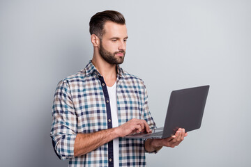 Portrait of attractive skilled focused bearded guy holding in hand using laptop typing email isolated over gray pastel color background
