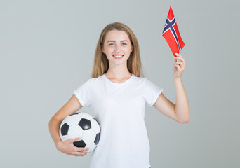 Wall Mural - Beautiful young woman with the flag of Norway and a soccer ball in her hands; looking at camera; isolated on gray background. Norwegian women's football.