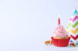 Delicious birthday cupcake with burning candle, sprinkles and party decor on white background, space for text