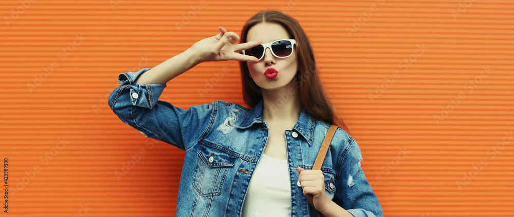 Portrait close up of young woman wearing a denim jacket with backpack posing on a orange background - obrazy, fototapety, plakaty 