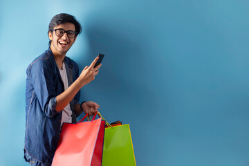 A young man standing with carry bags while holding his mobile. 	