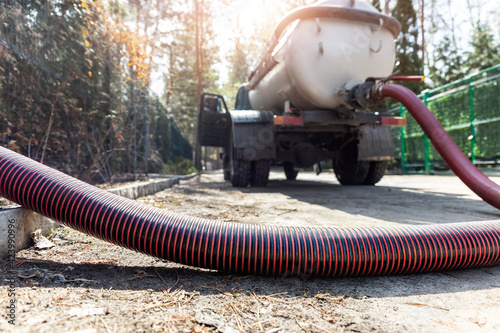 Obraz Dibond Close-up pipe hose of sewage truck car engine emptying home sewerage tank. Septic cleaning vacuum service and maintenance suburban countryside home. Suction vehicle cleaner machine pumping drainage