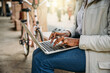 © loreanto - Young woman works at laptop sitting on a bench to send urgent work on the way to home with her bicycle after a day of work - Unrecognizable person - Concept of outdoor work