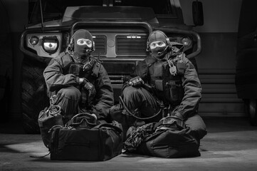 Two uniformed commandos sit in a hangar with a military truck in the background. SWAT concept.