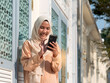 Pretty Asian Muslim woman in traditional clothing using mobile phone.