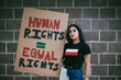 © Maskot - Portrait of female activist with human rights signboard against wall