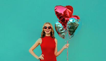 Portrait of happy smiling woman with bunch of red heart shaped balloons on a blue background