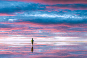 Wall Mural - A tourist stands in calm water, which reflects the incredible purple sunset sky. Landscape photography