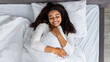 Satisfied young black woman waking up and hugging pillow
